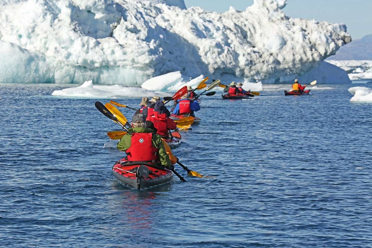 Kayakers pass icebergs in Greenland. 