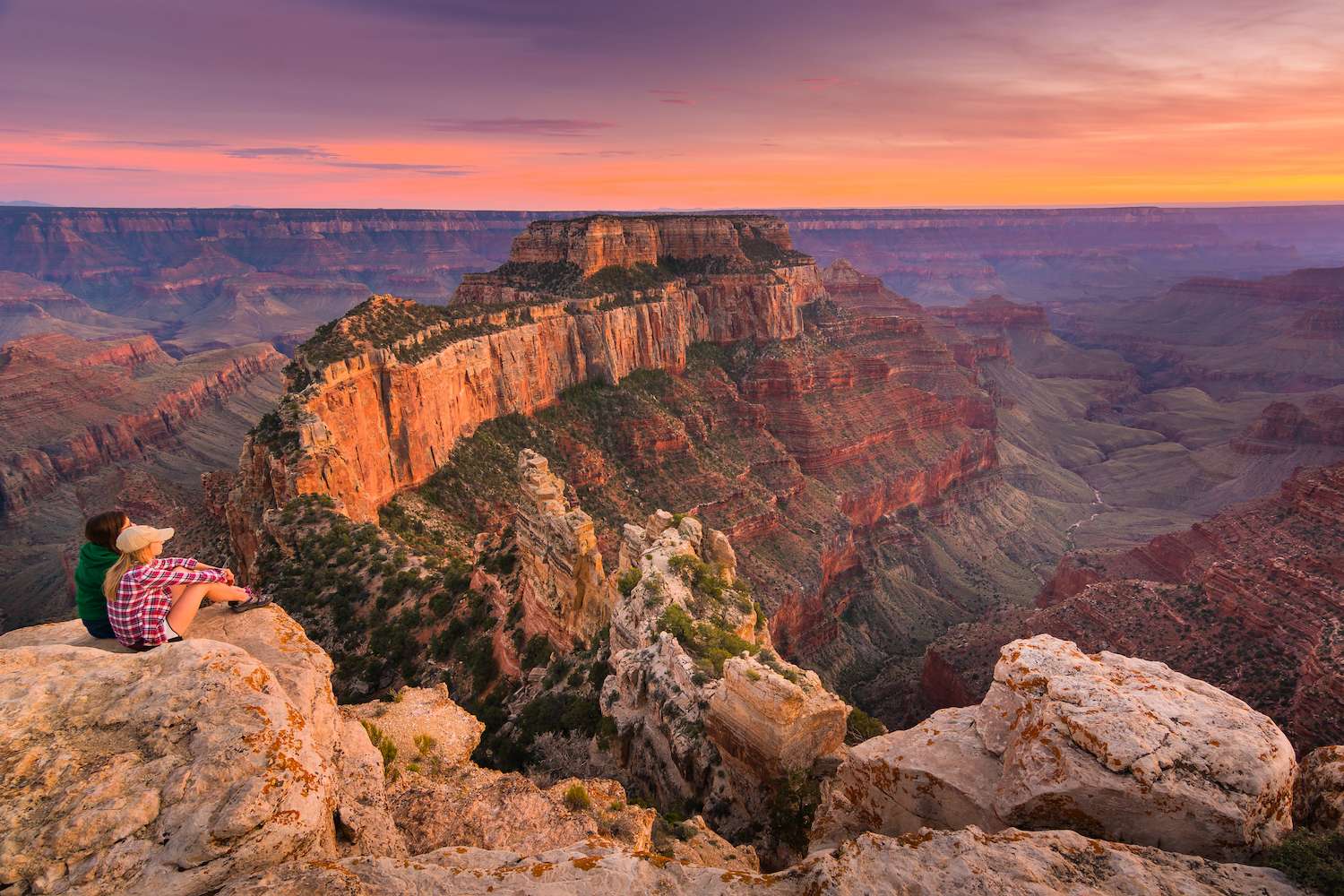 Two people sitting near the edge watching sunset at Grand Canyon National Park North Rim, USA. Grand Canyon National Park is one of the world's natural wonders.