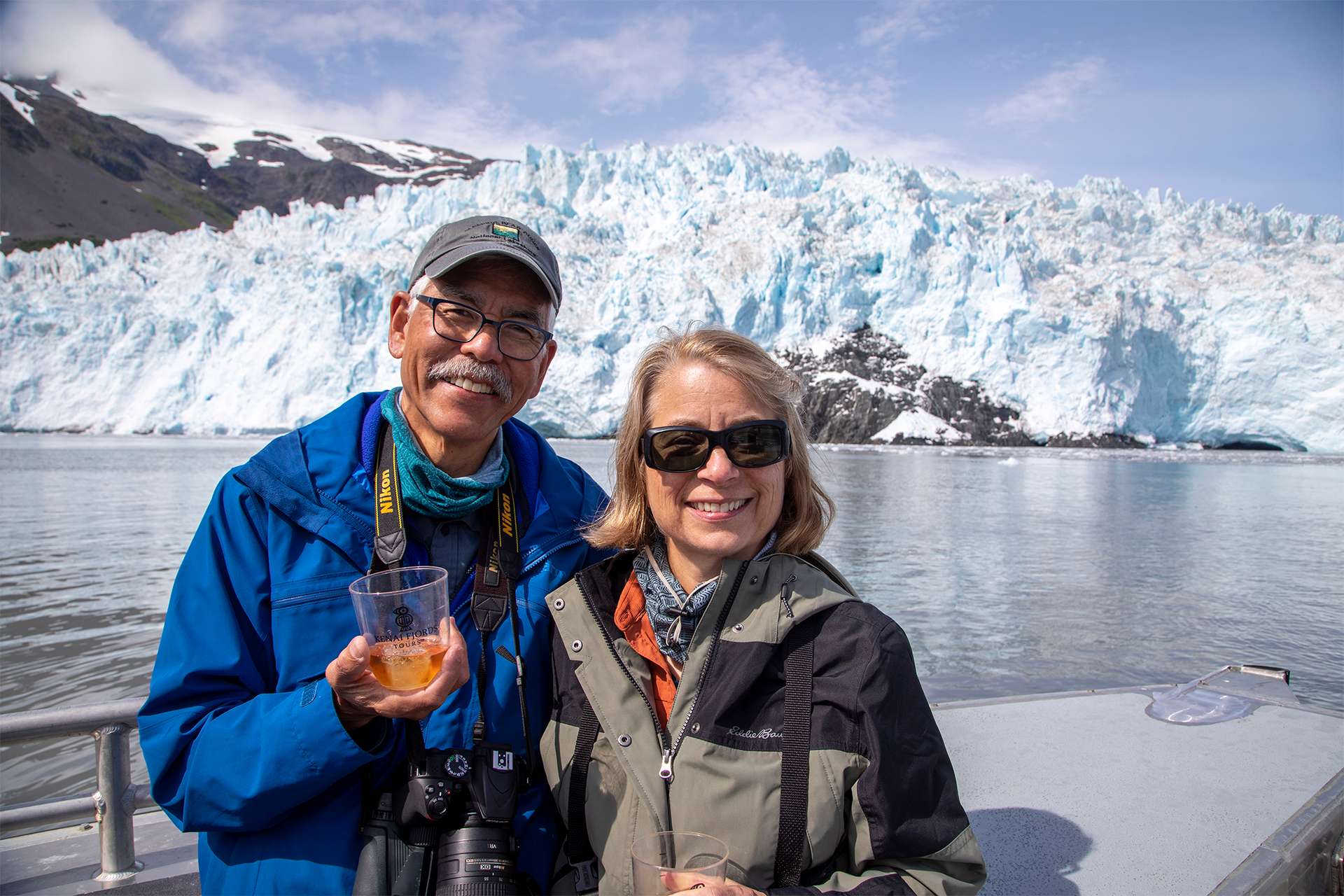 Travelers happily cheers with glass of wine aboard private board exploring glaciers in Alaska fjords