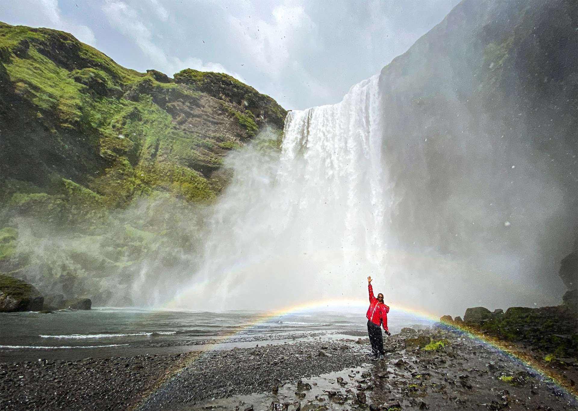 Traveler gleefully posing in front of Iceland waterfall and rainbow