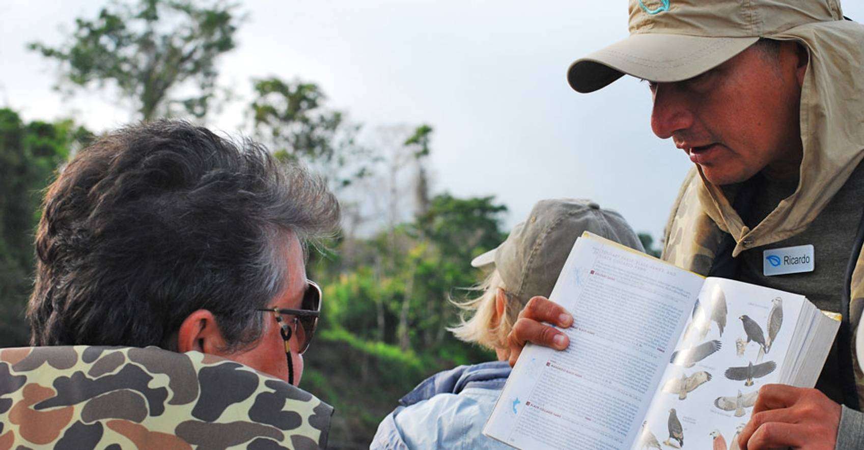 Guide showing his bird guide book to a traveler in the Amazon Rainforest