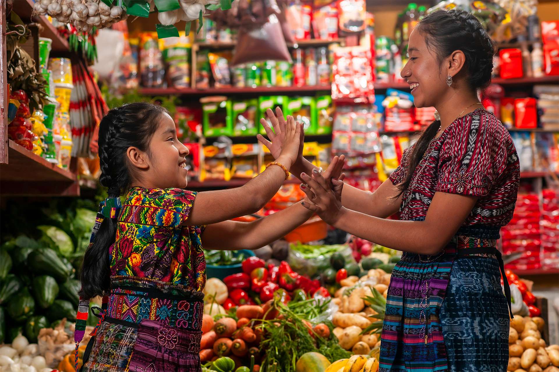 Food sovereignty two Indigenous girls laughing and playing in family grocery store Latin America produce fruit farming agriculture 