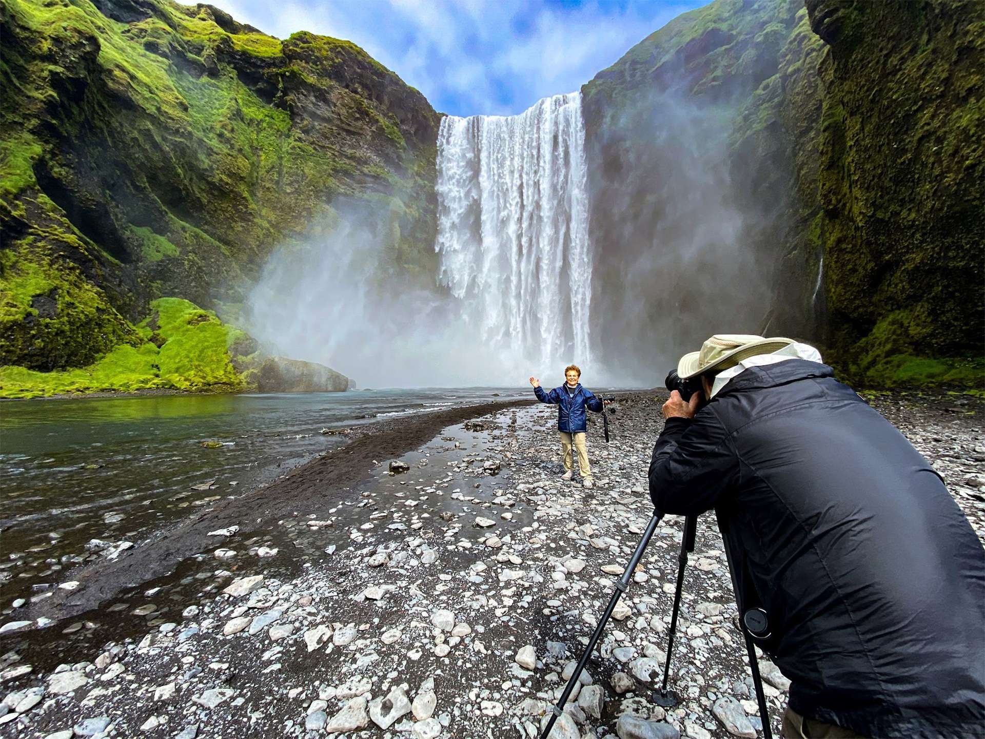 Nat Hab &amp; WWF traveler uses a tripod to compose a long exposure shot of his partner in front of Skogafoss waterfall in iceland