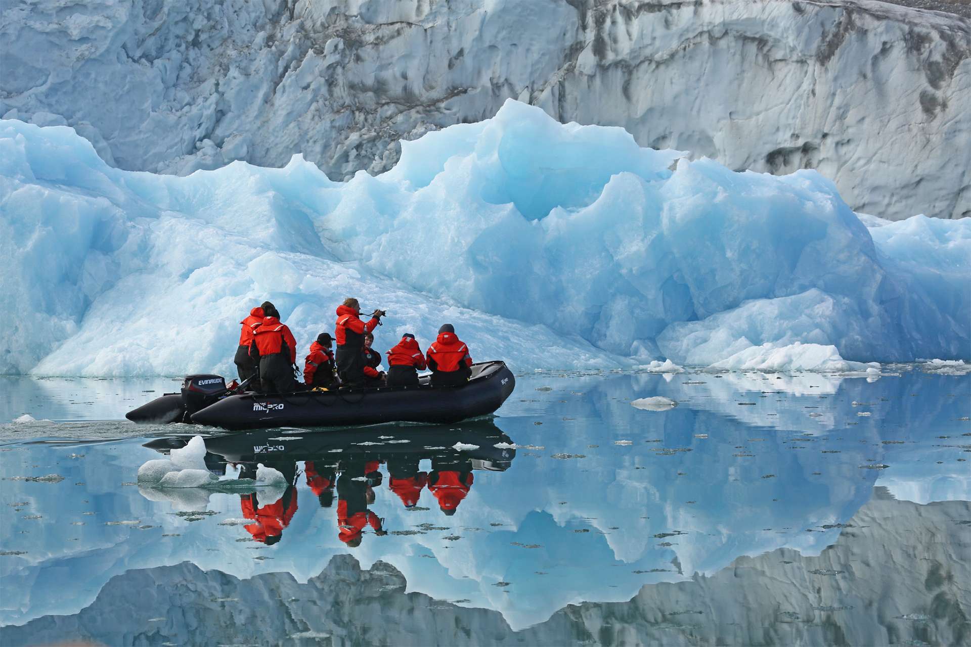 Travelers aboard zodiac travel through calm arctic waters in Greenland photographing icebergs and glaciers