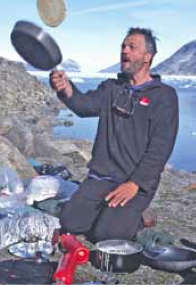 Olaf Malver flipping a pancake with mountain vistas behind him while camping